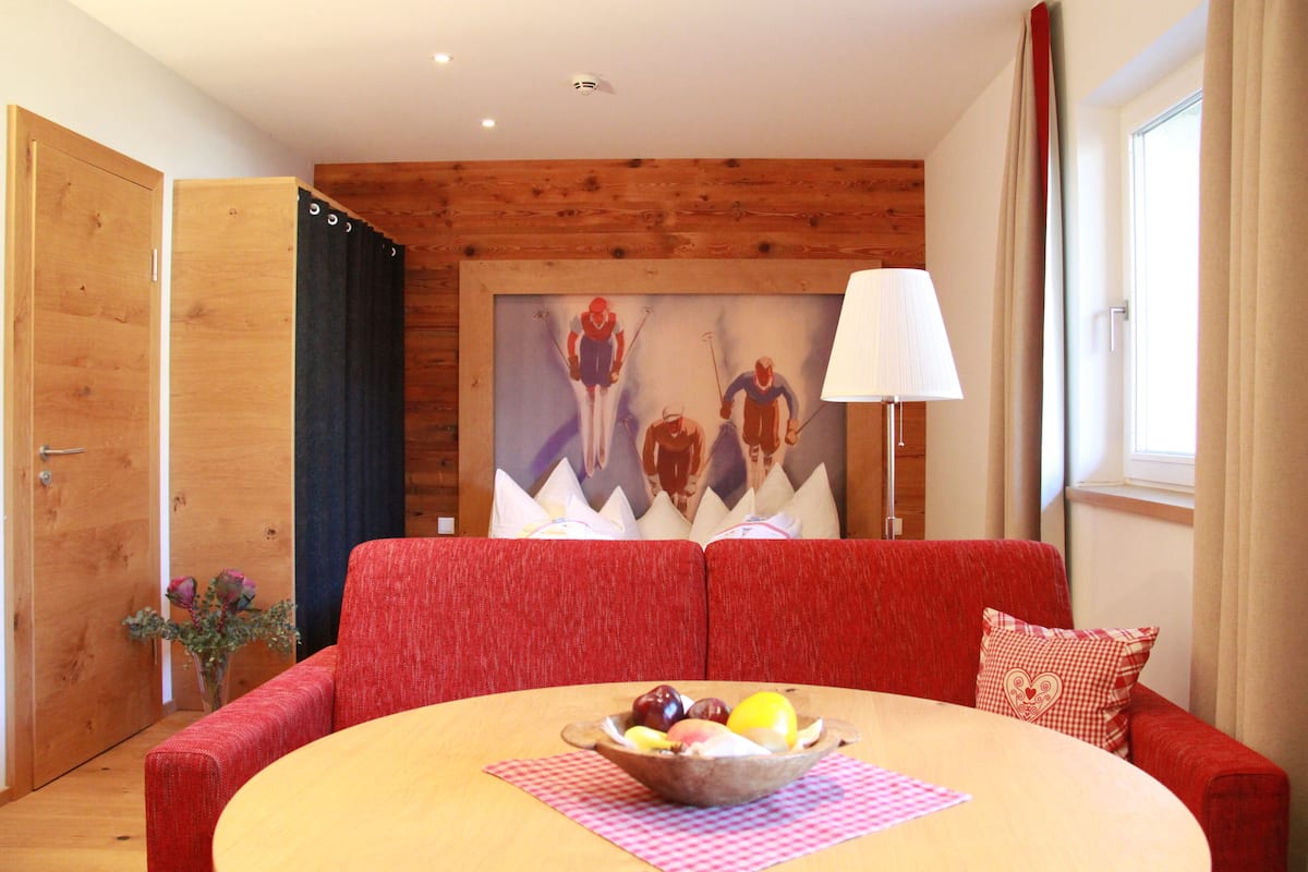 Una habitación con techo de madera, un sofá rojo, una mesa redonda con frutero y un cuadro en la pared.