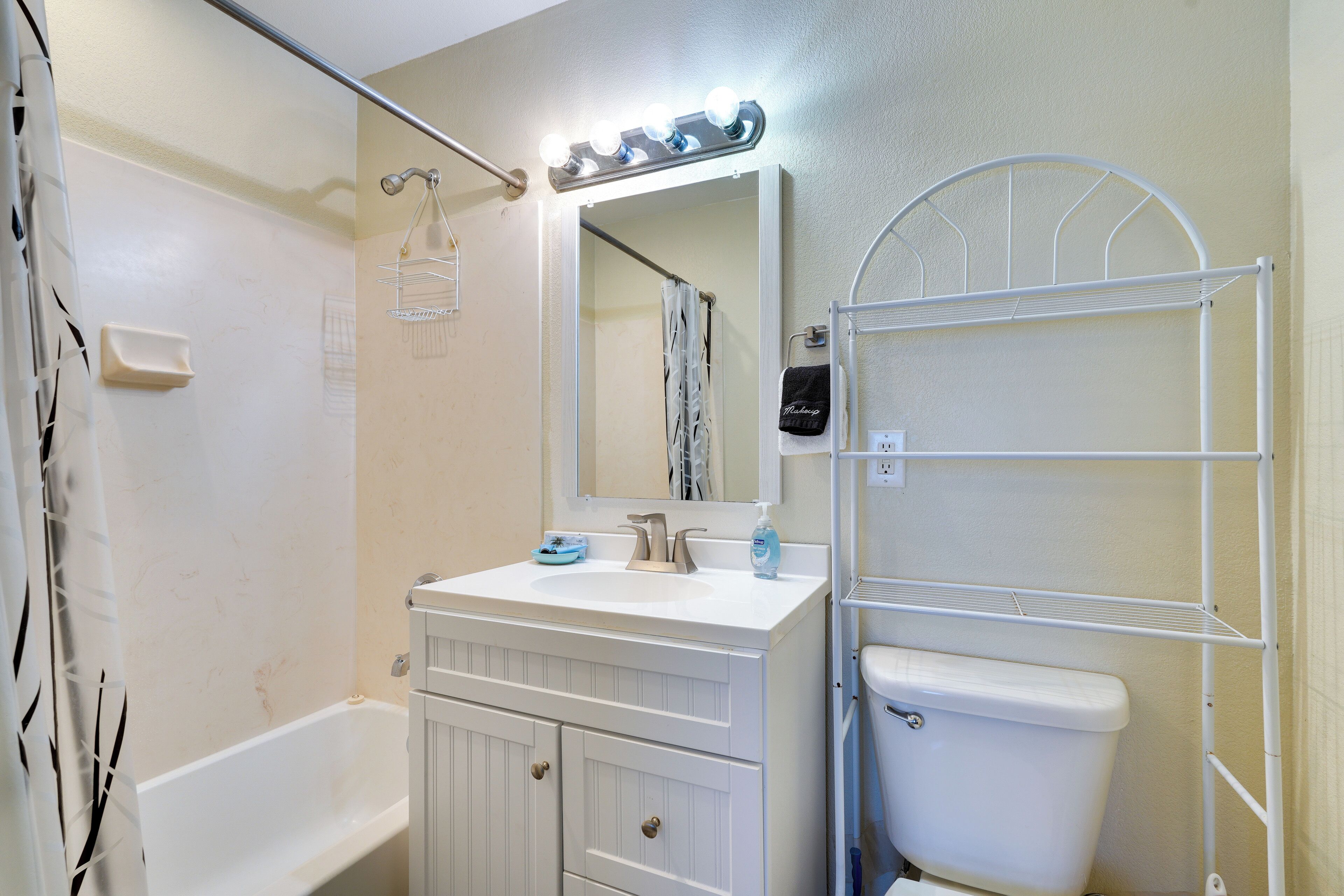 A bathroom with a bathtub, a sink, a toilet, and a mirror with lights.