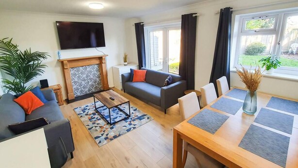A modern living room with a fireplace, sofa, coffee table, and dining table. - Impeccable 4-bed House in Cheltenham (Cheltenham)