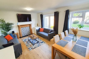 A modern living room with a fireplace, sofa, coffee table, and dining table. - Impeccable 4-bed House in Cheltenham (Cheltenham)