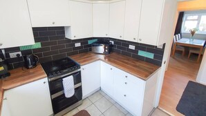 A compact kitchen with white cabinets, black and teal backsplash tiles, a black stove, and a wooden countertop. - Impeccable 4-bed House in Cheltenham (Cheltenham)