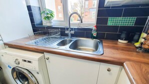 A compact kitchen with a built-in washing machine, a double sink, and a window with a view of the outside. - Impeccable 4-bed House in Cheltenham (Cheltenham)