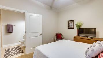 Un dormitorio con una cama, un televisor sobre un tocador de madera, una puerta y un baño con inodoro y toallero.