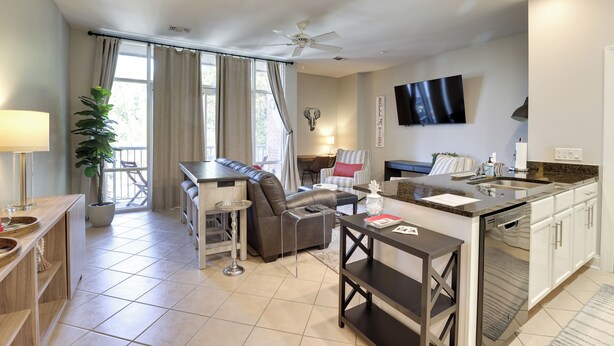 A modern living room with a sofa, dining table, and kitchen area with a dishwasher. - Tuscaloosa Condo: Steps to Bryant-denny Stadium! (Tuscaloosa)