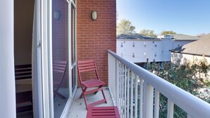 A balcony with a red chair and a small table, a brick wall, and a white railing. - Tuscaloosa Condo: Steps to Bryant-denny Stadium! (Tuscaloosa)