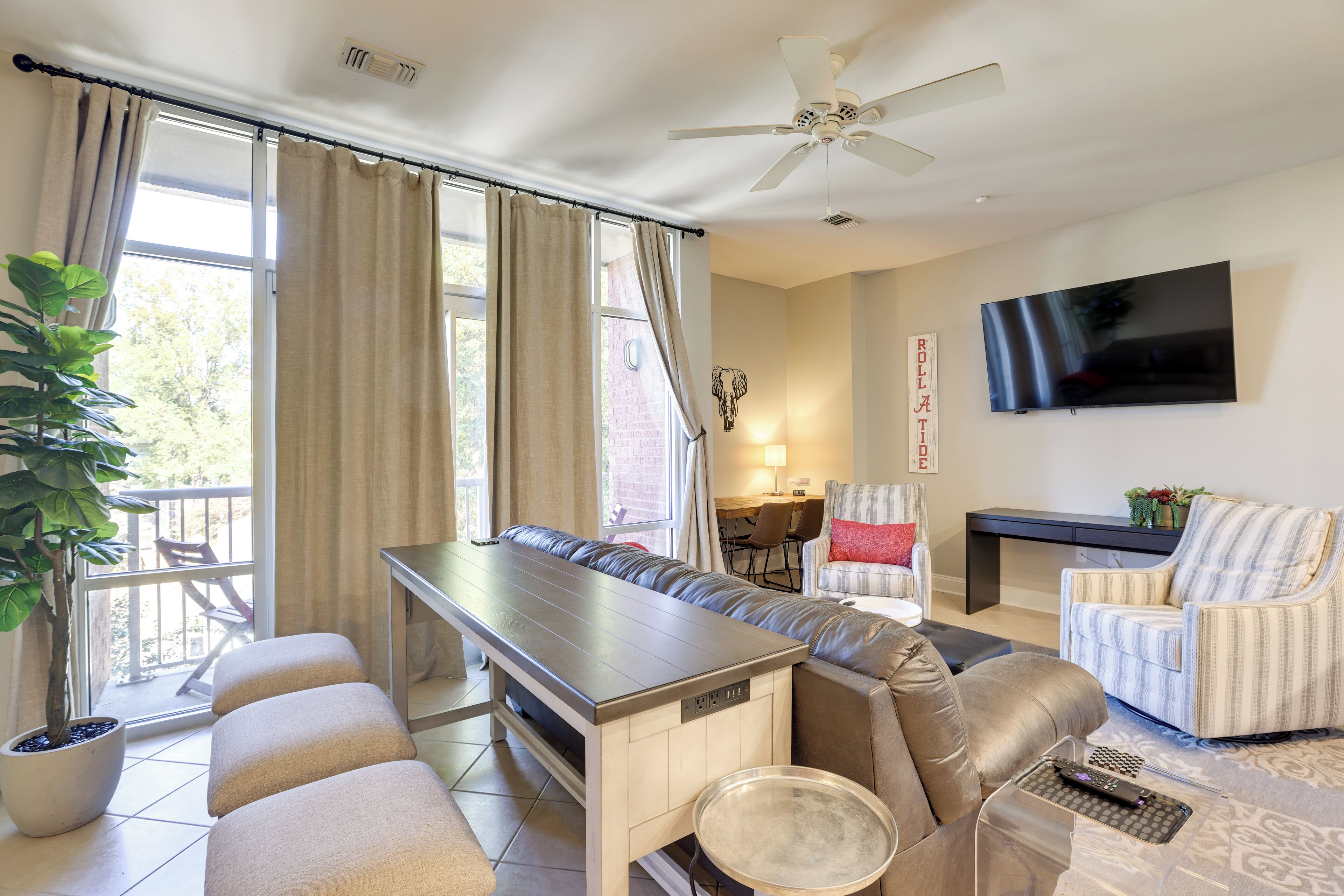 A modern living room with a sofa, armchair, dining table, and a television mounted on the wall.