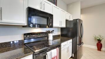 A kitchen with white cabinets, a stainless steel refrigerator, a microwave, and a stove.