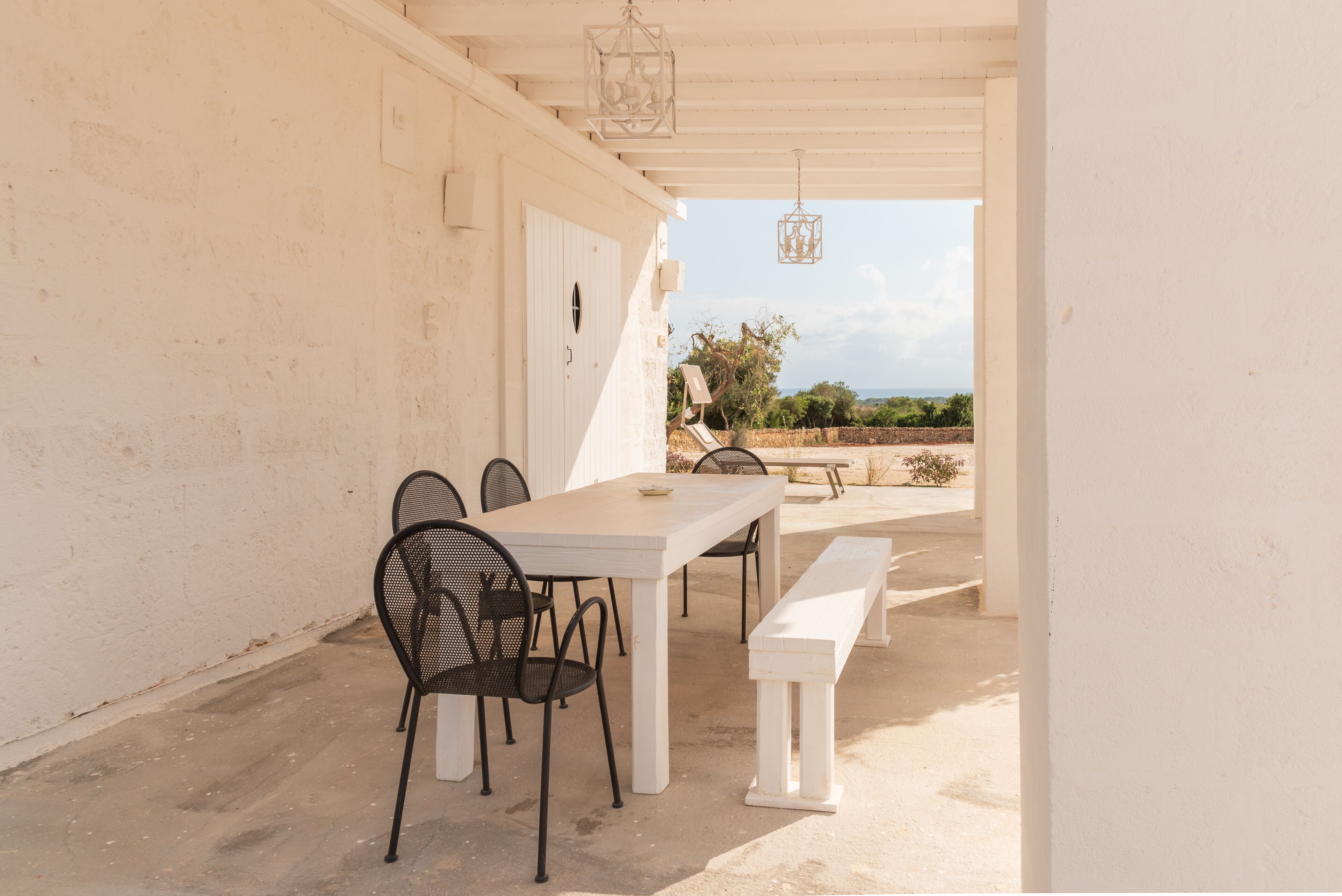An outdoor patio with a white table and chairs, a bench, and hanging lanterns.