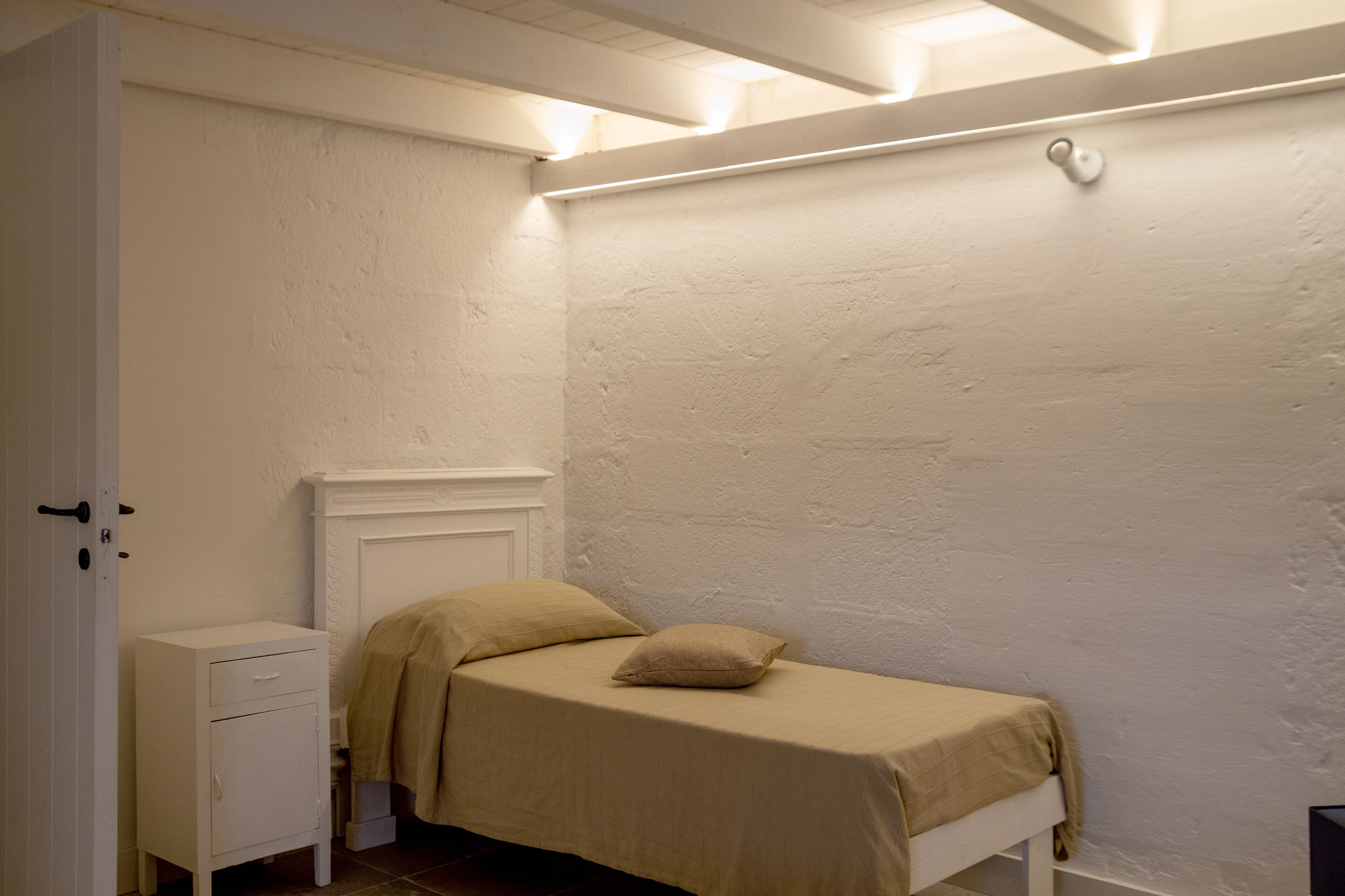 Una habitación pequeña con cama individual, cabecera de madera, mesita de noche y una puerta.