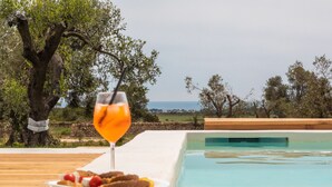 A poolside setting with a glass of orange drink, a plate of food, and a view of the sea. - Masseria Scaledda (Manduria)