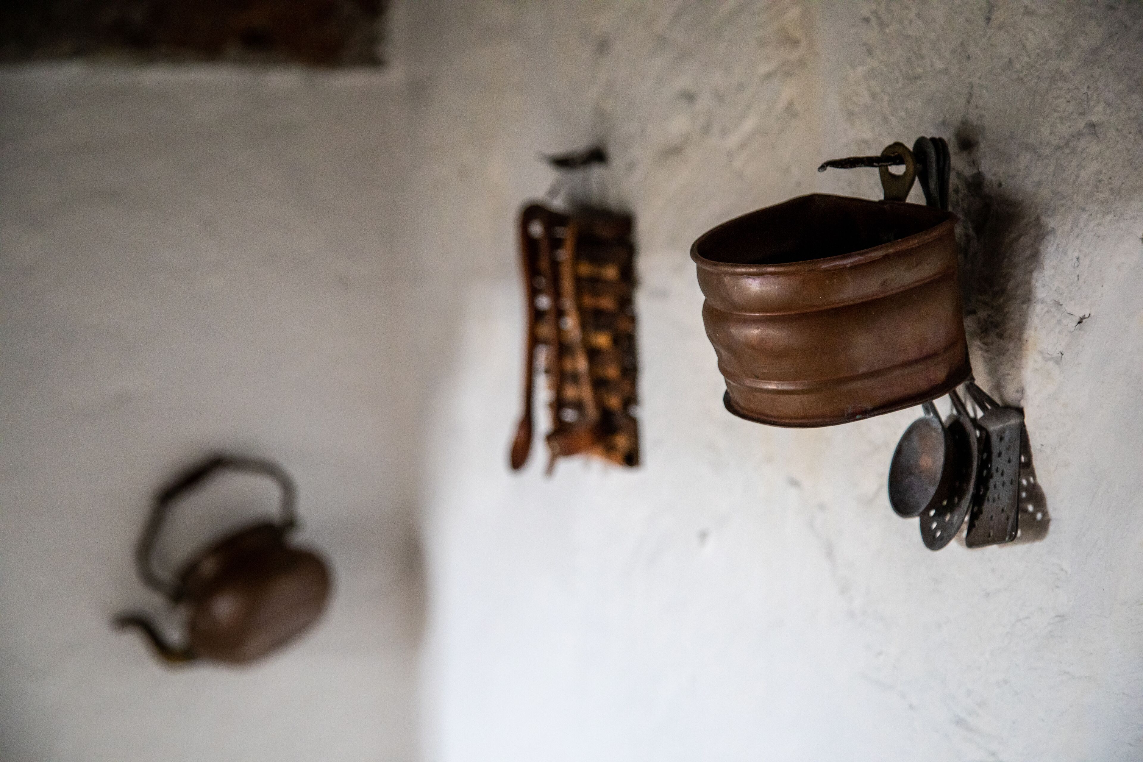 A kitchen with a hanging pot rack, a kettle, and a colander.