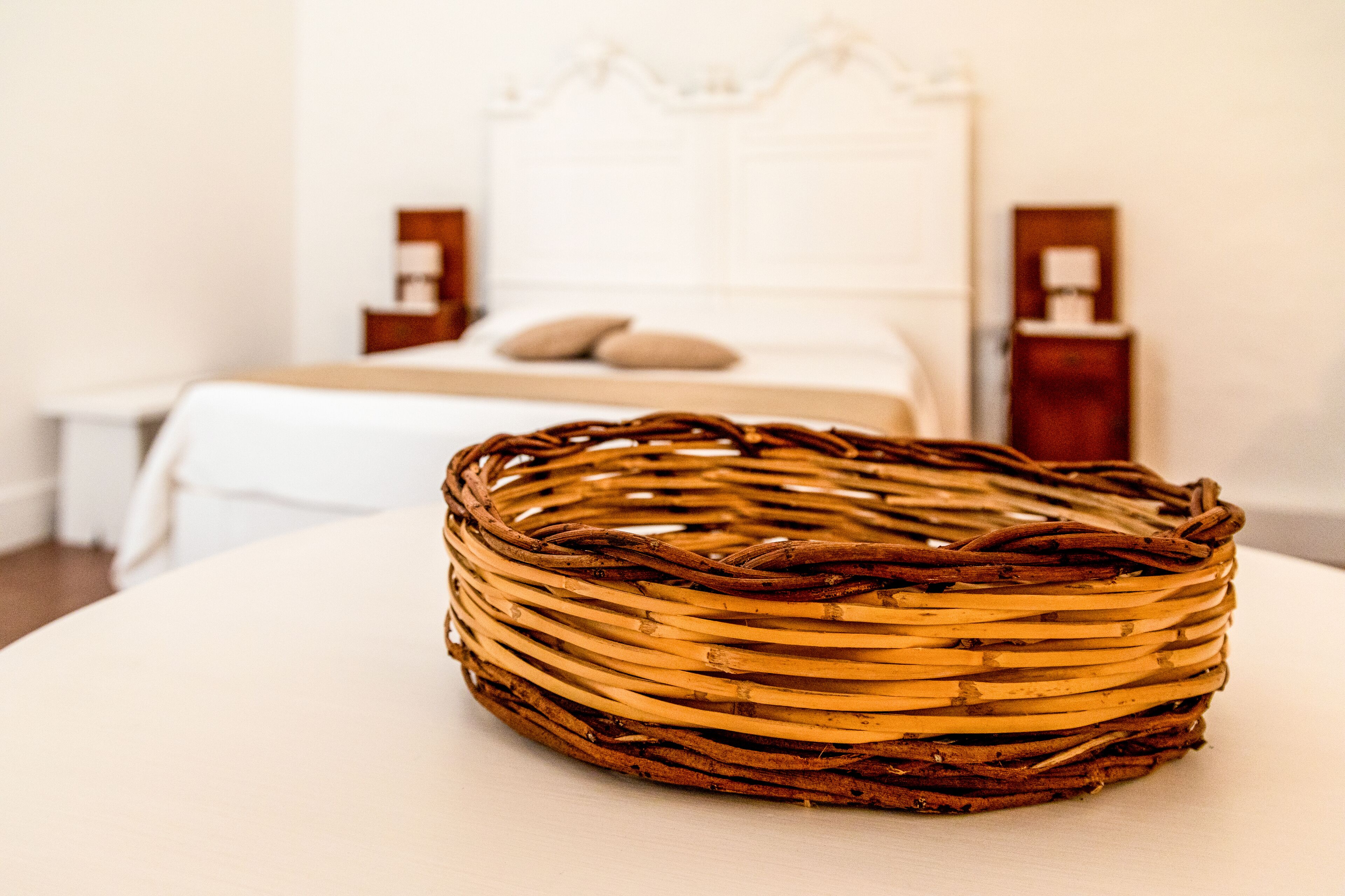 A wicker basket on a round table in a hotel room with a bed and nightstands in the background.