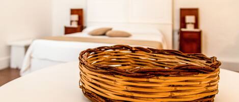 A wicker basket on a round table in a hotel room with a bed and nightstands in the background.