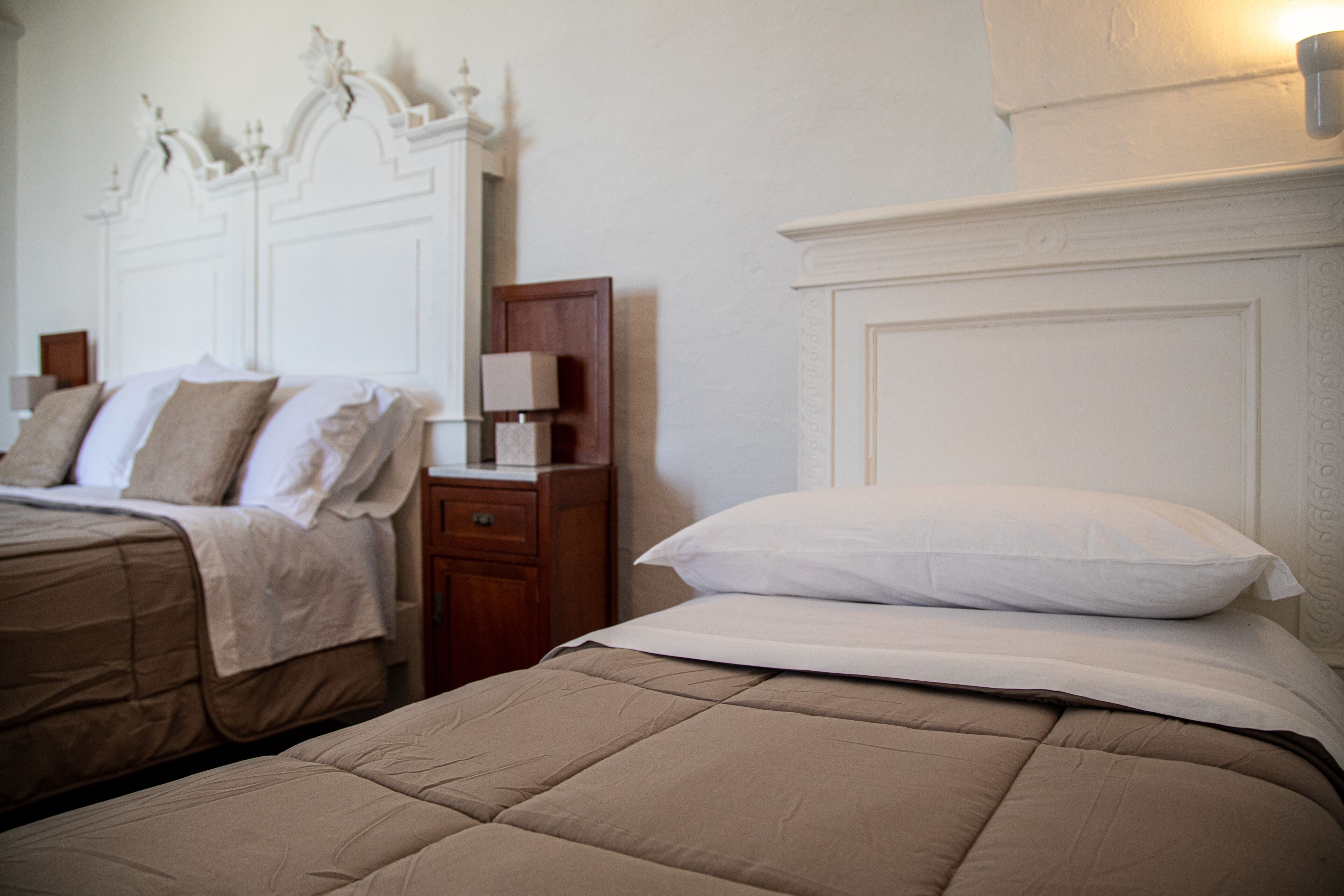 Habitación de hotel con dos camas, una mesita de noche y una lámpara de pared.