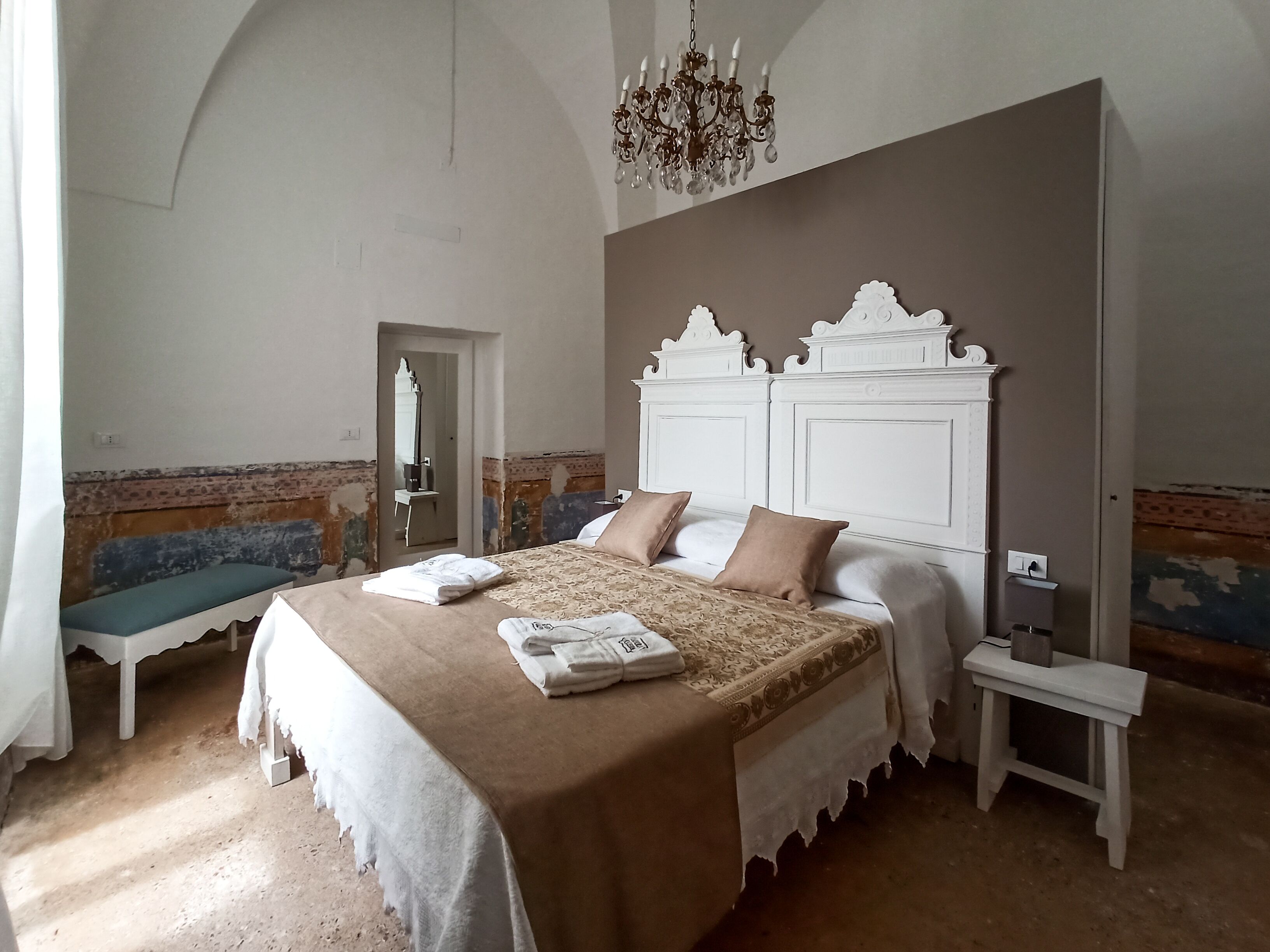 Ein Schlafzimmer mit einem großen Bett, einer Bank, einem Nachttisch und einer Kandelaber.