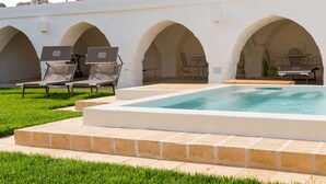 A swimming pool with a white tiled deck, surrounded by a low stone wall with arches. There are lounge chairs and a table under the arches. - Masseria Scaledda (Manduria)