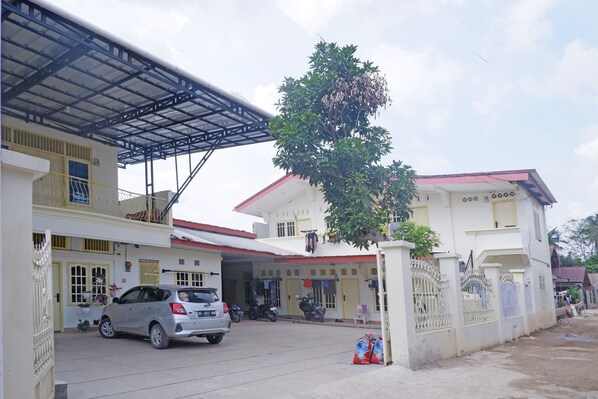 A building with a covered entrance, a gated driveway, and parked vehicles. - OYO Life 92632 Kost Pondok Kito (Jambi)