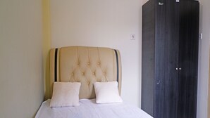 Un lit avec une tête de lit capitonnée et deux oreillers, une armoire en bois foncé et un mur sobre avec un interrupteur.
