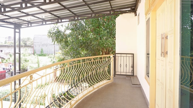 Un balcon fermé, doté d’une rambarde en métal, d’un sol carrelé et offrant une vue sur la verdure et les bâtiments en arrière-plan.