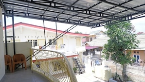 Un espace extérieur abrité, doté d’un escalier en métal, de deux chaises en plastique et d’un arbre.
