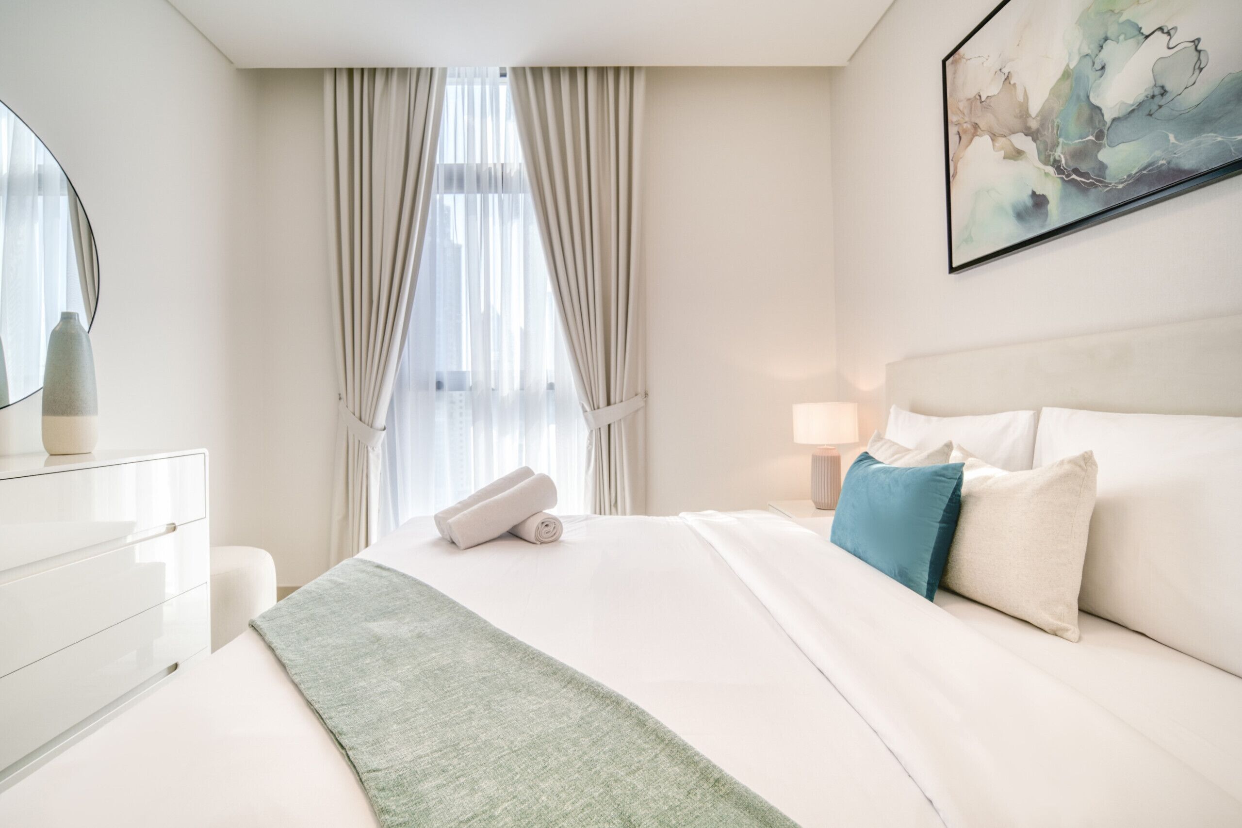 Een moderne hotelkamer met een groot bed, een nachtkastje met een lamp, een spiegel en een schilderij aan de muur.