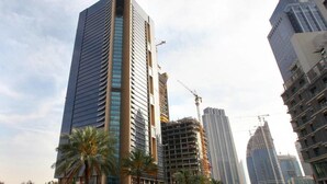 Un rascacielos alto y moderno con un diseño elegante, rodeado de otros edificios de gran altura y palmeras.
