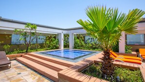 Un área de piscina moderna al aire libre, con un jacuzzi, terraza de madera y sillones de descanso.