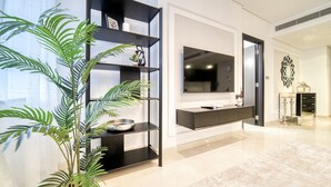 Una sala de estar moderna con un televisor grande, un estante negro y una planta en maceta.