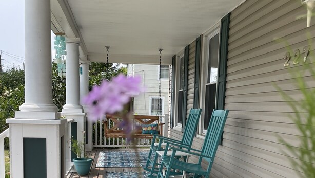 A wooden porch with teal rocking chairs and a patterned rug.