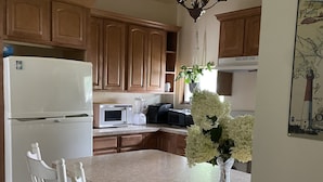 A kitchen with wooden cabinets, a white refrigerator, a microwave, and a dining area with white chairs.