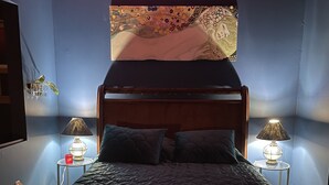 A bedroom with a wooden bed, two bedside tables with lamps, a wall-mounted artwork, and a window with blinds.