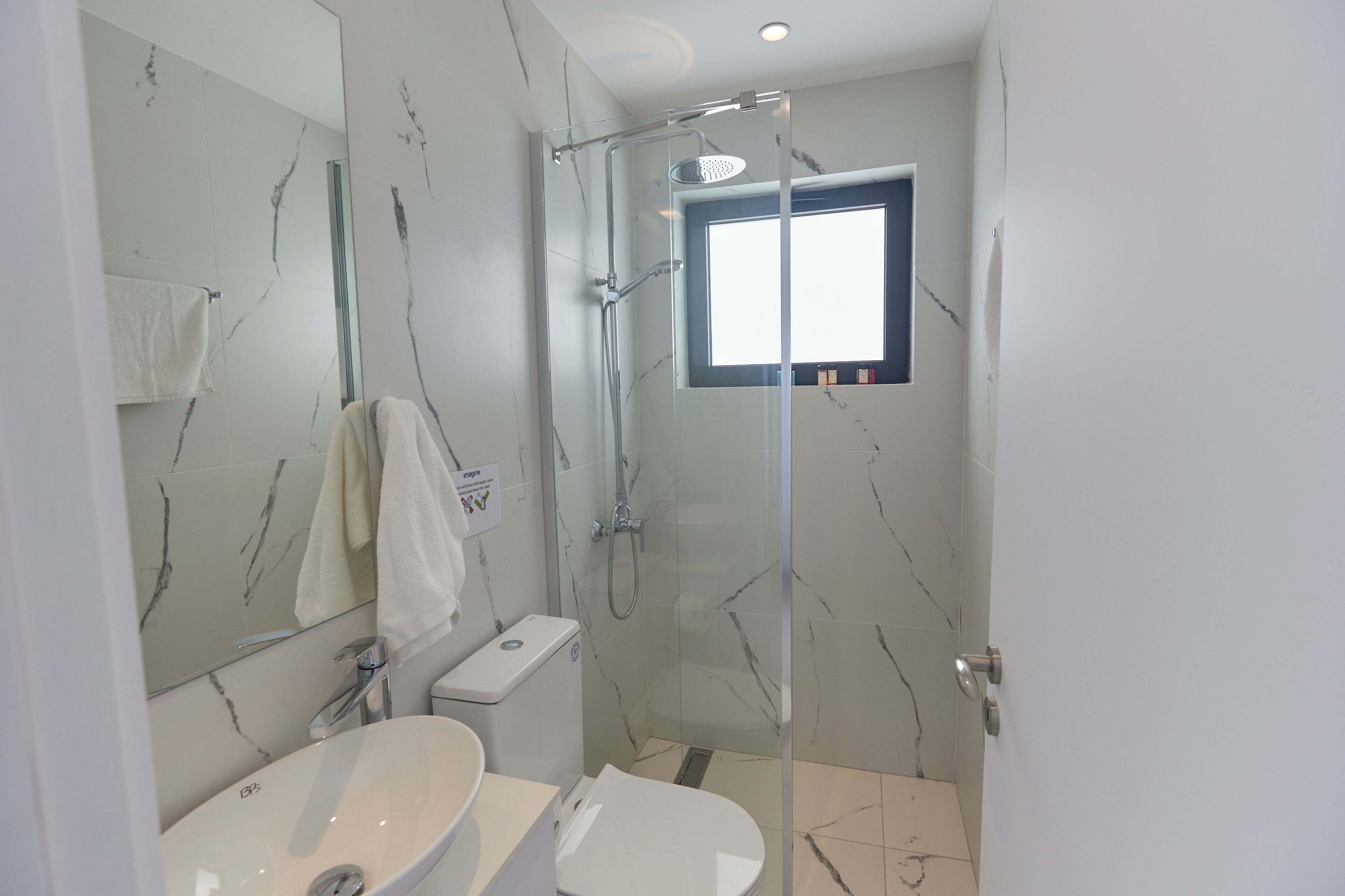 A modern bathroom with a glass-enclosed shower, a white sink, and a toilet.
