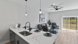 A modern kitchen with a white marble countertop, stainless steel sink, and pendant lights.