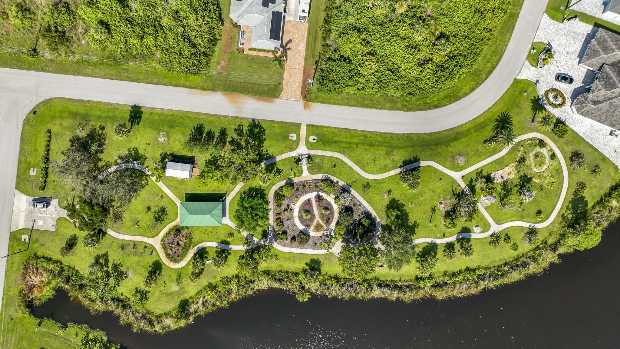 Une vue aérienne d’un parc avec des allées, un jardin circulaire central et un petit bâtiment.