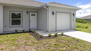 A single-story house with a front door, a garage, and a small front yard with young trees.
