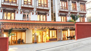 A traditional building with multiple balconies and large windows, featuring intricate architectural details and a view of mountains in the background. - Hotel Mayto (Thimphu)