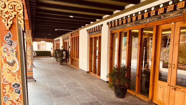 A covered corridor with tiled flooring, wooden doors, and decorative wall panels. - Hotel Mayto (Thimphu)