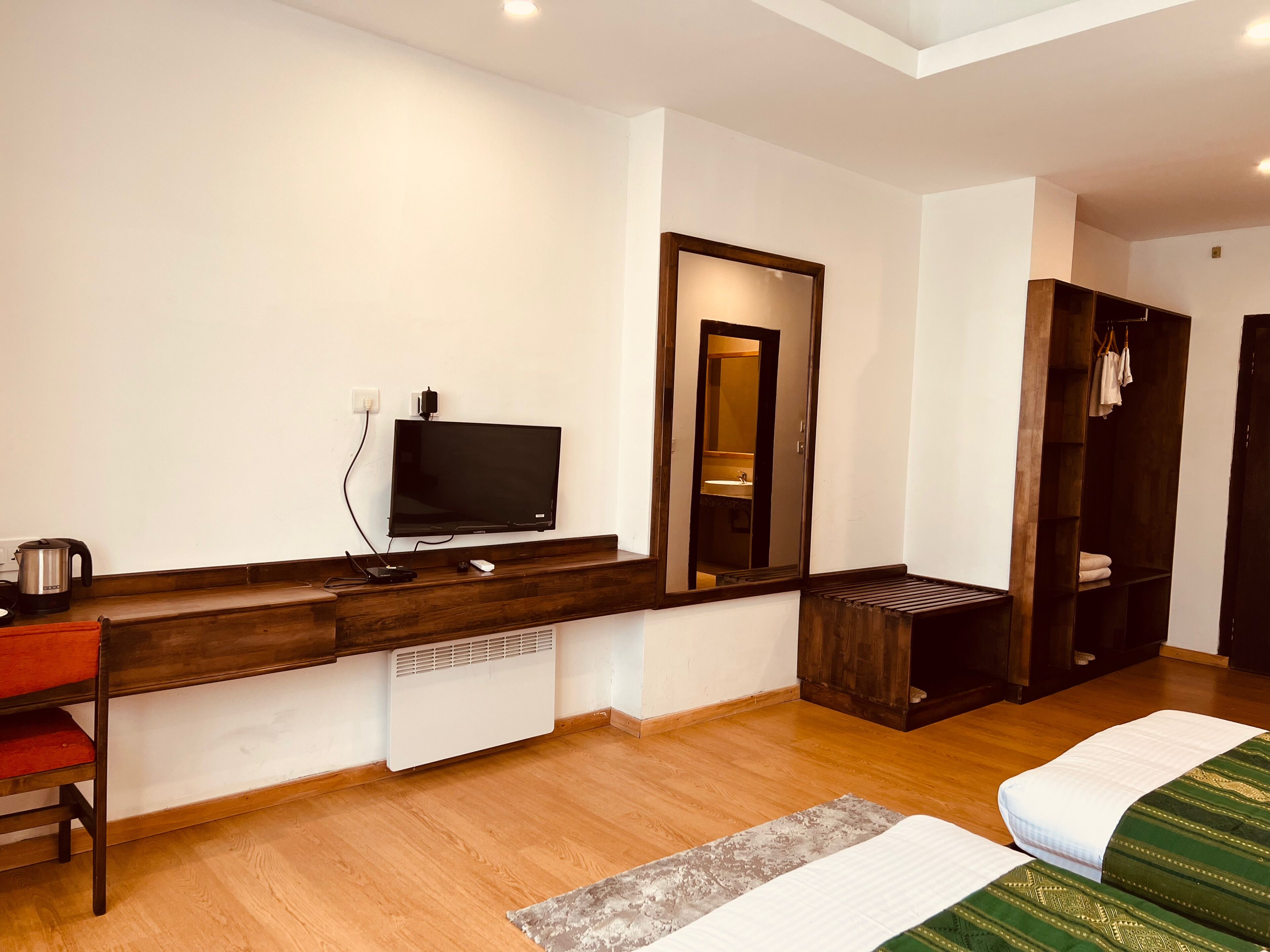 Habitación de hotel con escritorio de madera, televisión, espejo, armario y cama con colcha estampada.