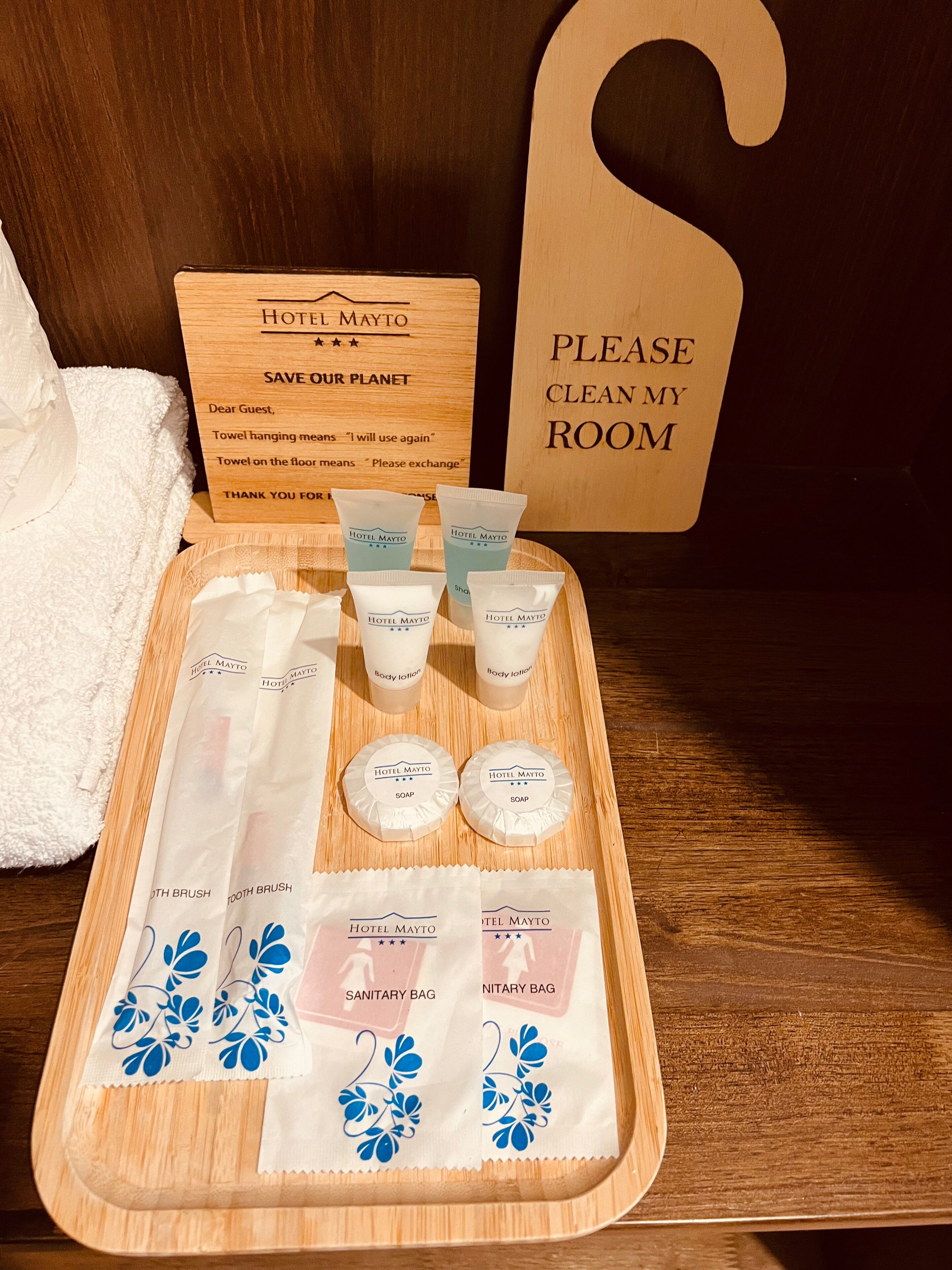 A hotel room with a wooden tray containing toiletries, a towel, and a sign instructing guests to clean their room.