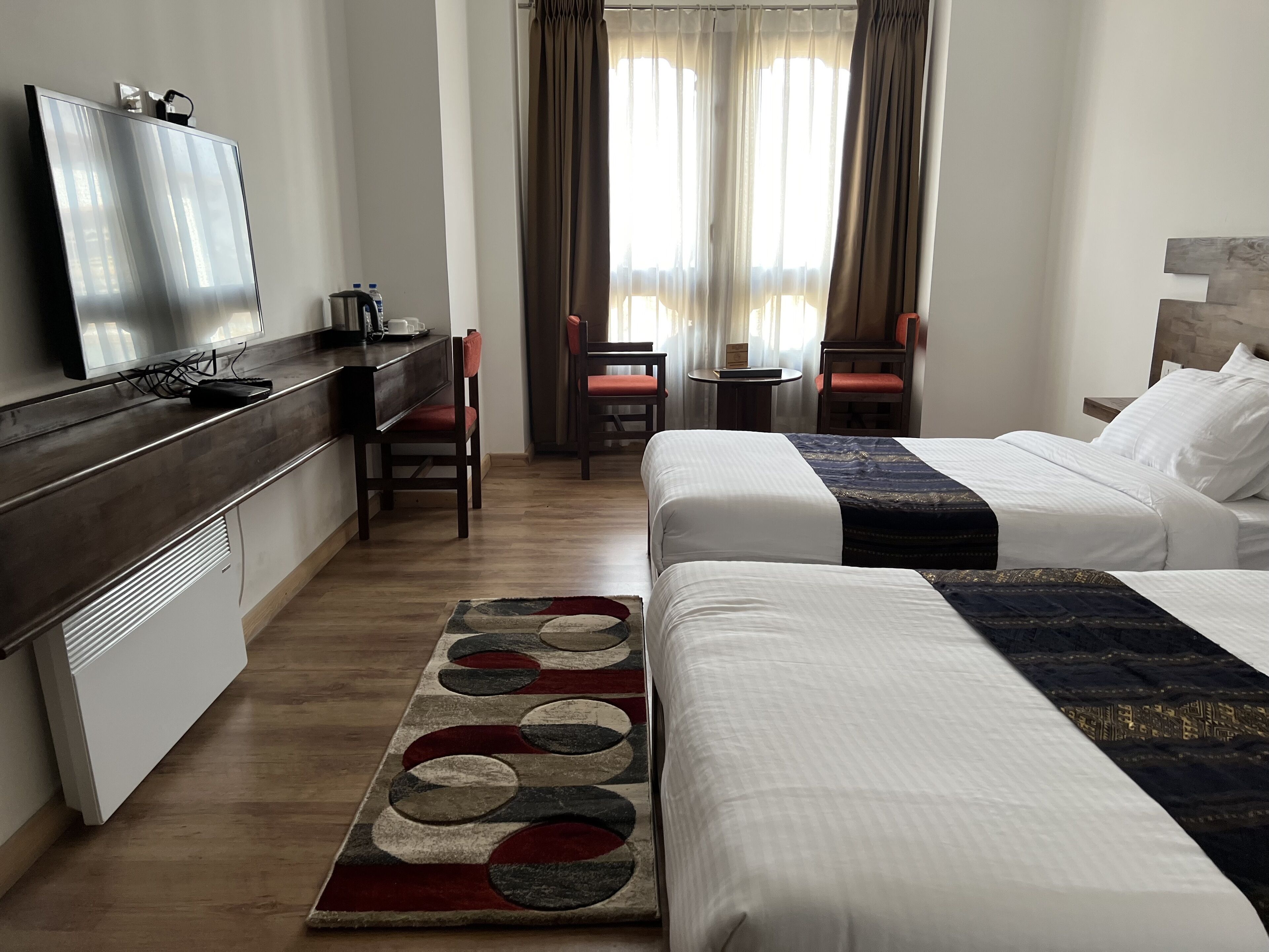 A hotel room with two beds, a desk with a chair, a television, and a small table with a chair.