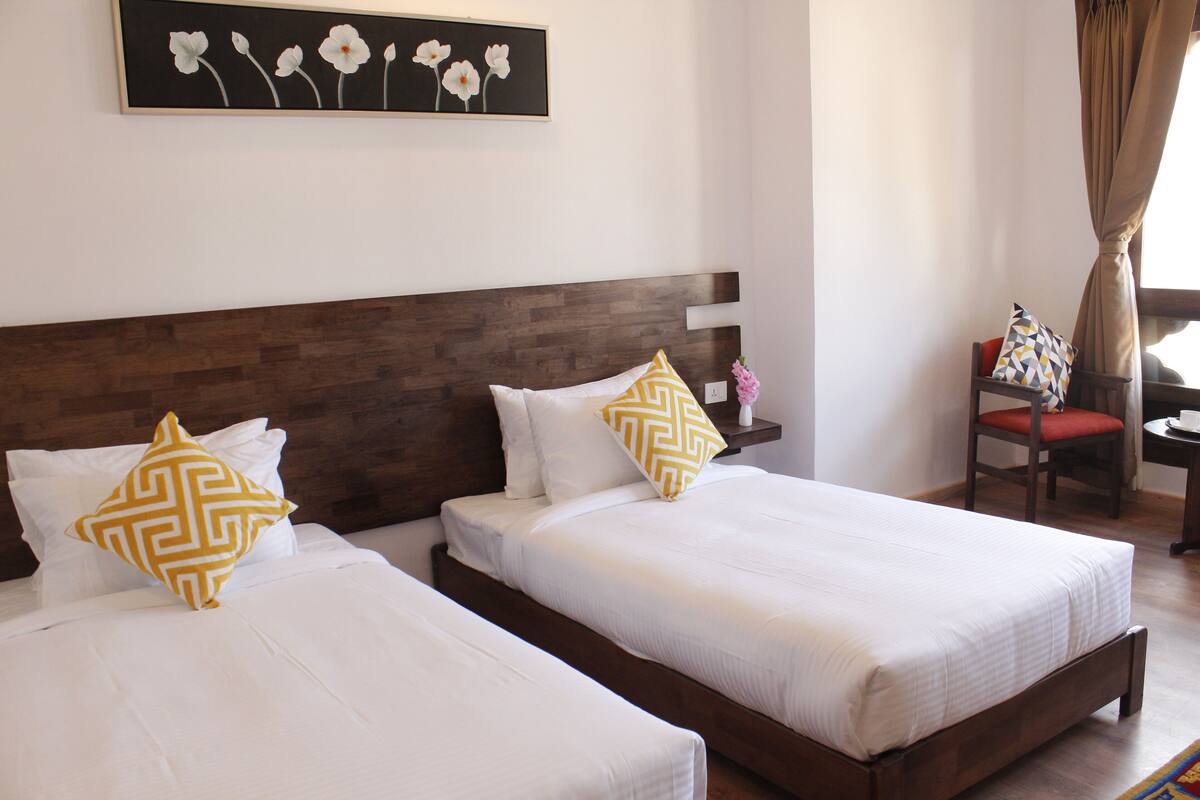 A hotel room with two beds, a wooden headboard, a painting on the wall, and a chair with a cushion.