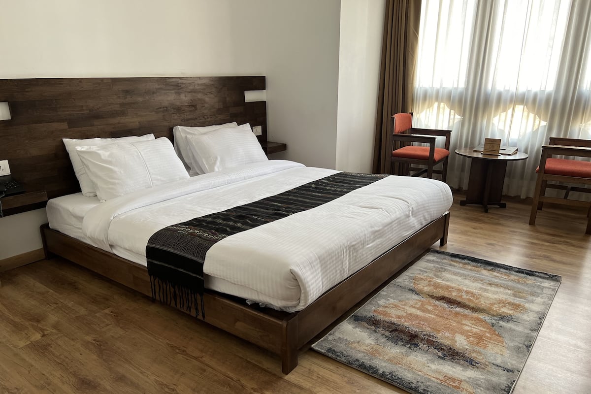A neatly made bed with a wooden headboard, a bedside table with a phone, and a small table with a book and a sign.