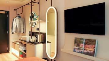 A modern hotel room with a bed, a vanity with a mirror, a flat-screen TV, and a picture of a scenic location.