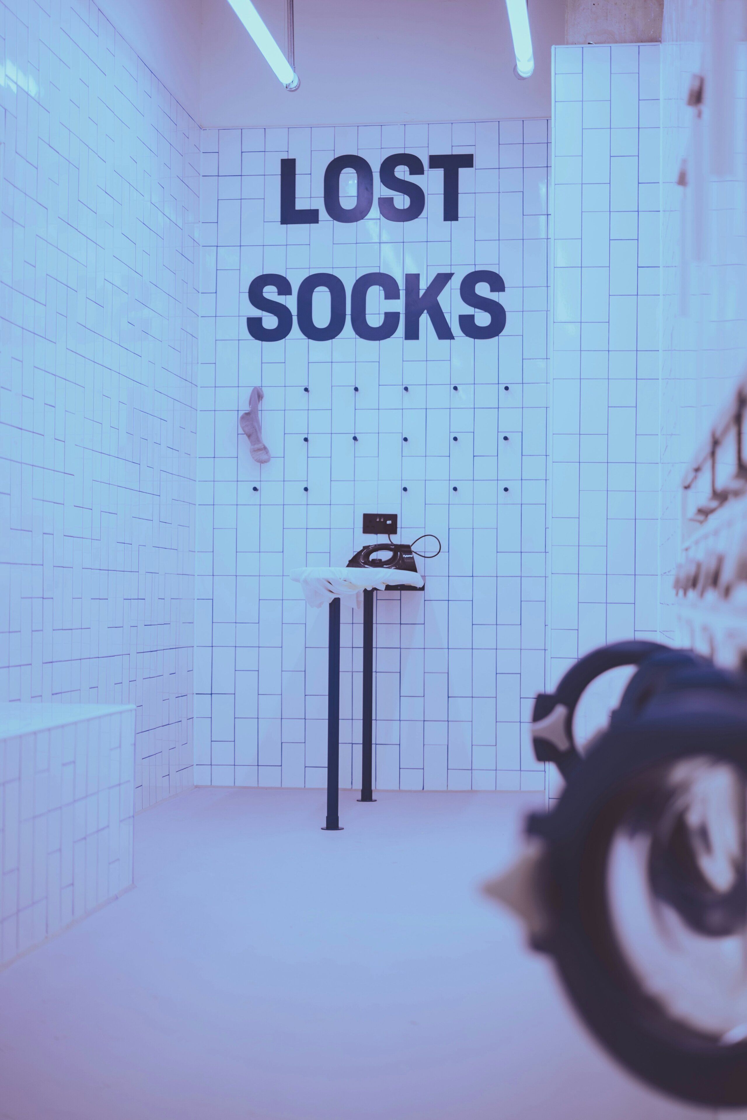Una habitación con un muro de diseño en cuadrícula, un cartel que dice 'LOST SOCKS', un zapatero y un par de auriculares.