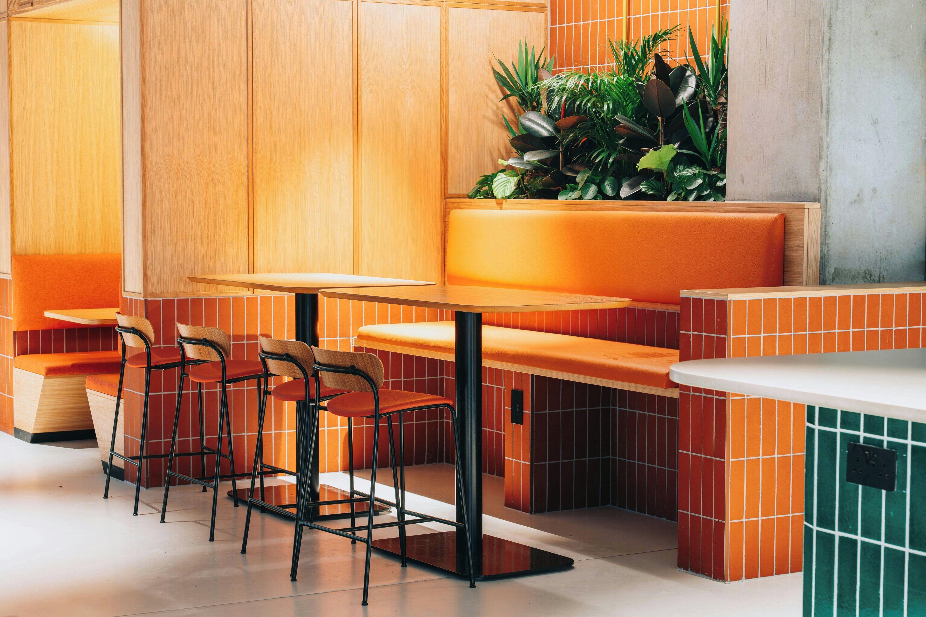A modern restaurant interior with wooden paneling, orange seating, and a green accent wall.