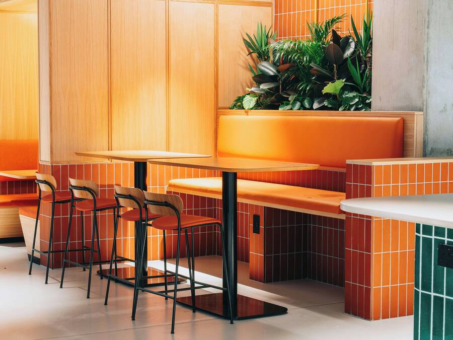 A modern restaurant interior with wooden paneling, orange seating, and a green accent wall.