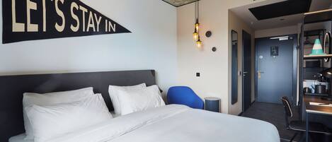 Una habitación de hotel con una cama grande, un escritorio, una silla y un cartel que dice 'LET'S STAY IN'.