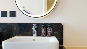 A bathroom with a white sink, a round mirror, and three bottles of Zenology hand wash.