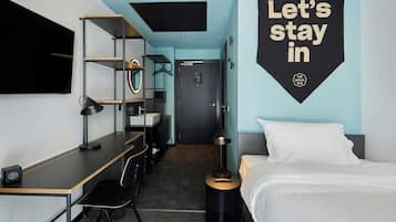 Una habitación de hotel moderna con escritorio, silla, cama y un cartel en la pared.