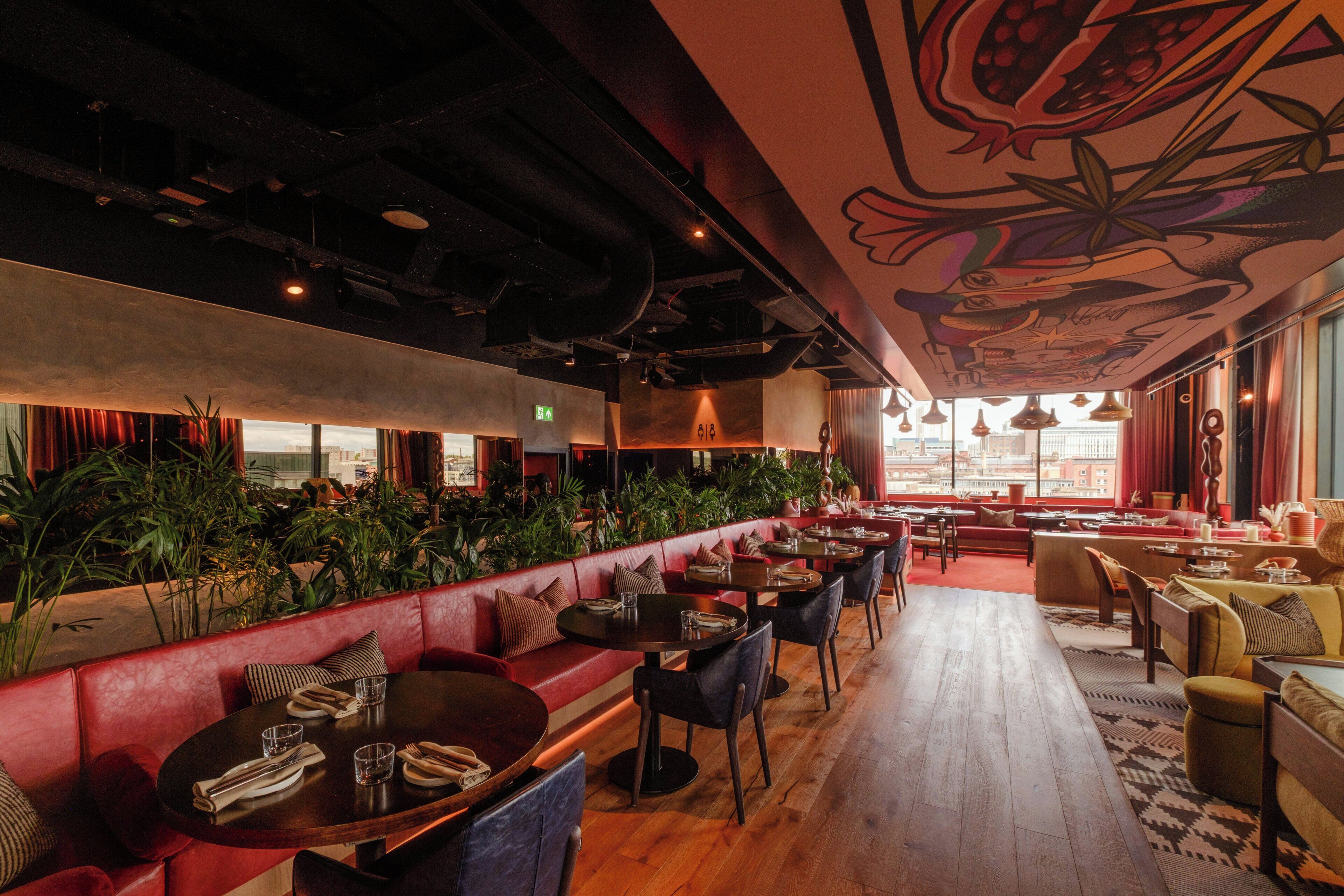 Un restaurante con una barra larga, cabinas y un techo alto con un mural.